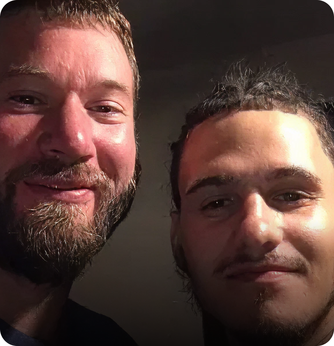 Two men smiling in a dimly lit room.